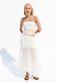 White lace two-piece outfit featuring a strapless top with asymmetrical design and a long skirt with sheer overlay. Worn with black flip-flops.