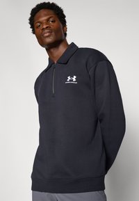 Tmavomodrý sweatshirt s štvrťovým zipsom, dlhými rukávmi a golierom. Na hrudi sa nachádza biele logo Under Armour. Hladká textúra.