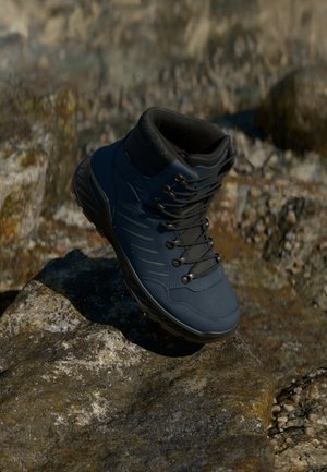 Donkerblauwe wandelschoen met een gevoerde kraag, rubberen zool, metalen oogjes en een soepele synthetische bovenkant met zijaccenten.
