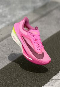 Różowe sneakersy Nike Zoom Fly z teksturowaną siateczką, ciemnoróżowym swooshem i jasnymi żółtymi akcentami. Lekka, amortyzująca podeszwa do biegania.