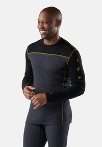 Thermisch shirt met lange mouwen, met een zwart bovenstuk en een donkergrijze onderkant, geaccentueerd met gele stiksels en iconen op de mouwen.
