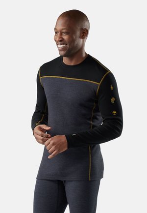 Thermisch shirt met lange mouwen, met een zwart bovenstuk en een donkergrijze onderkant, geaccentueerd met gele stiksels en iconen op de mouwen.