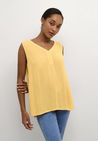 Yellow sleeveless blouse with a V-neck and a subtle textured finish, featuring a front placket and a relaxed fit. Paired with light denim jeans.