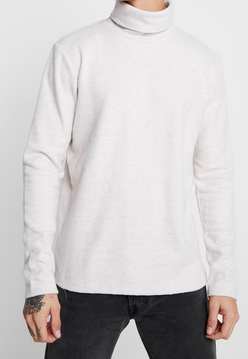 Jasnoszary sweter z golfem wykonany z teksturowanej tkaniny, z długimi rękawami i prążkowanym wzorem, zestawiony z ciemnymi dżinsami.