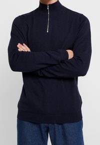 Marine gekleed zip-nek trui van lichtgewicht stof met gebreide manchetten en zoom. Soepele textuur, aansluitend ontwerp en minimalistische zilveren ritsdetail.