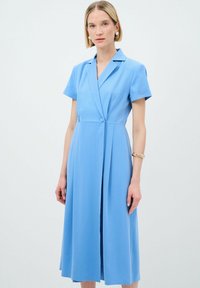 Robe bleu clair à manches courtes, col montant, fermeture à boutons et design plissé. Tissu lisse avec une coupe mi-longue.