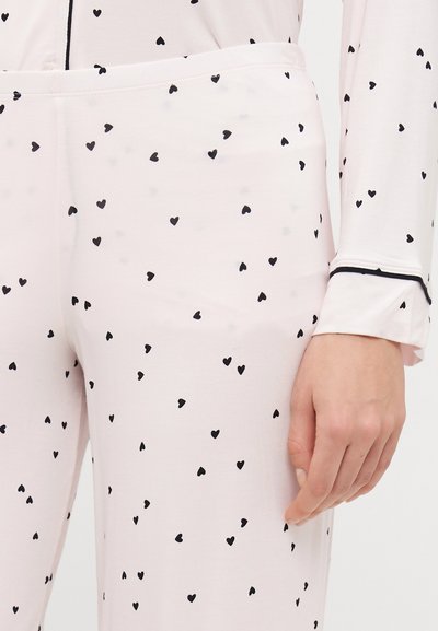 Ροζ πιτζάμα με απαλή υφή, διακοσμημένη με μικρά μαύρα σχέδια καρδιάς, αντίθεση στις ραφές των μανικιών και ελαστική ζώνη για άνεση.