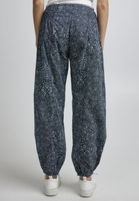 Pantalons amples à motif bleu foncé avec un design paisley blanc ; taille élastique et chevilles resserrées ; portés avec des baskets blanches.