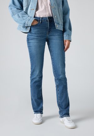 Donkerblauwe denim jeans met een rechte pasvorm, middelhoge taille en een lichte wassing. Gecombineerd met een lichtblauwe denim jas en witte sneakers.