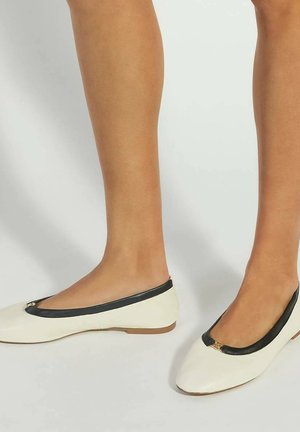 Ballet flats blanches avec des bordures noires, bout rond et un petit accent doré à l'avant. Texture lisse et design de profil bas.