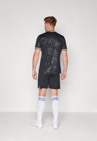 Sort atletisk trøje med blomsterdesign, kombineret med sorte shorts. Hvide knæstrømper med blå striber. Spidse hvide sko.