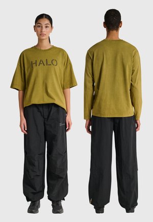 Widok z przodu i z tyłu dwóch modeli ubranych w oliwkowozielone koszulki HALO oraz luźne czarne spodnie i czarne trampki na szarym tle.