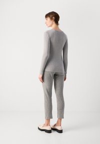 Grå ribbestrikket langermet topp kombinert med teksturerte grå skråbukser. Modellen har på seg kremfargede slip-on sko med tykke svarte såler.