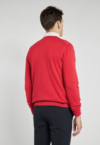 Czerwony sweter z okrągłym dekoltem, z ribbowaną mankietami i dołem. Miękka dzianina. Nosi się na białej koszuli z kołnierzykiem w małe kropki.