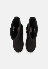 Botas negras hasta el tobillo con un forro suave y texturizado, un exterior liso y un diseño de puntera redondeada. La parte superior tiene un detalle de costura decorativa.