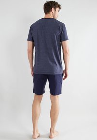 Marineblau gestreiftes T-Shirt mit kurzen Ärmeln, kombiniert mit marineblauen Shorts, ausgestattet mit einer lockeren Passform und weichem Baumwollmaterial, barfuß getragen.