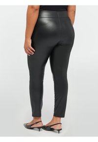 Leggings neri in ecopelle con una texture liscia, vita alta e un design aderente. Indossati con tacchi neri con borchie.