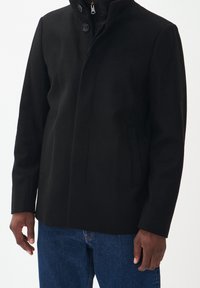 Svart ullblandad kappa med hög krage, två framfickor och enkel knappstängning. Har en slät textur och skräddarsydd passform.