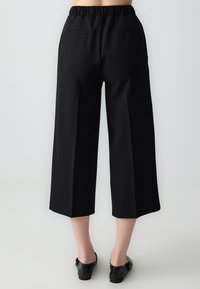 Pantalons larges noirs en tissu texturé, taille élastique et deux poches arrière. Pas de motifs ou d'accents visibles. Bas à ourlet plat.