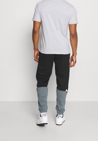 Grå t-shirt och svarta joggingbyxor med turkosa detaljer. Joggingbyxorna har åtsittande passform och elastiska muddar. Vita sneakers fulländar outfiten.