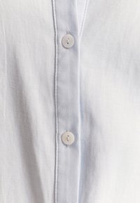 Light blue shirt in soft fabric featuring a button-up front with white buttons and subtle texture, emphasizing a classic design.