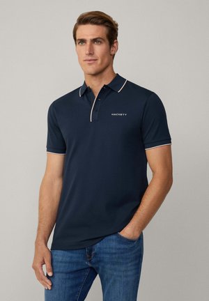 Navyblauw polo-shirt met een contrasterende kraag, een drieknoopsluiting en het "HACKETT" logo geborduurd op de borst. Korte mouwen, soepele textuur.