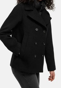 Černý kabát ve stylu peacoat, vyrobený z vlněné směsi, s dvouřadým zapínáním na knoflíky, širokými klopami a postranními kapsami. Hladká textura a přiléhavý střih.