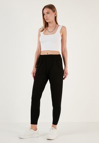Zwarte joggers met een elastische tailleband, gecombineerd met een witte geribbelde crop top. De look wordt compleet gemaakt met witte sneakers.