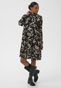 Mustast ja beežist mustriga pikad varrukad kleit volditud äärega, millel on kõrge kaelus ja lõdva lõikega, kombineeritud põlvekõrguste mustade saapadega.