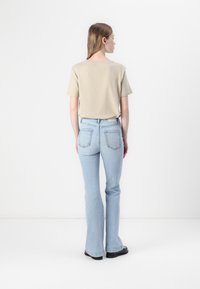 Beige kortermet t-skjorte kombinert med lyseblå flagrende jeans. Antrekket har en avslappet passform og har et minimalistisk design. Svarte sko er synlige.