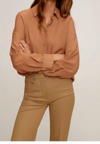 Blouse marron à manches longues avec boutons, en tissu léger, assortie à un pantalon beige taille haute avec une texture lisse et une coupe ajustée.