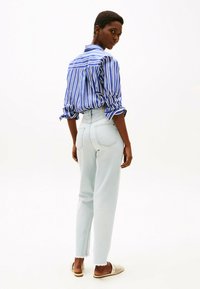 Jeans azzurri a vita alta con orli grezzi abbinati a una camicia aderente a righe blu e bianche, con maniche arrotolate.