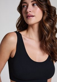 Black ribbed bralette with a scoop neckline and wide straps. Fabric texture is soft and form-fitting, suitable for comfortable wear.