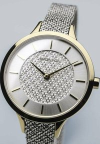 Silver mesh strap watch with a gold-tone bezel, textured silver dial, and gold hour markers. Features minimalist design and sleek shape.