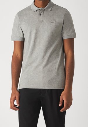 Mann trägt ein hellgraues, kurzärmeliges Poloshirt mit Kragen und einem kleinen BOSS-Logo auf der Brust, kombiniert mit einer schwarzen Hose.
