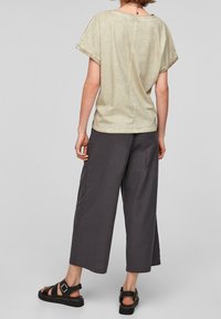Jasnooliwkowa bluzka z krótkim rękawem w połączeniu z ciemnoszarymi spodniami typu wide-leg. Bluzka ma luźny krój i miękką fakturę; spodnie charakteryzują się prostym designem.