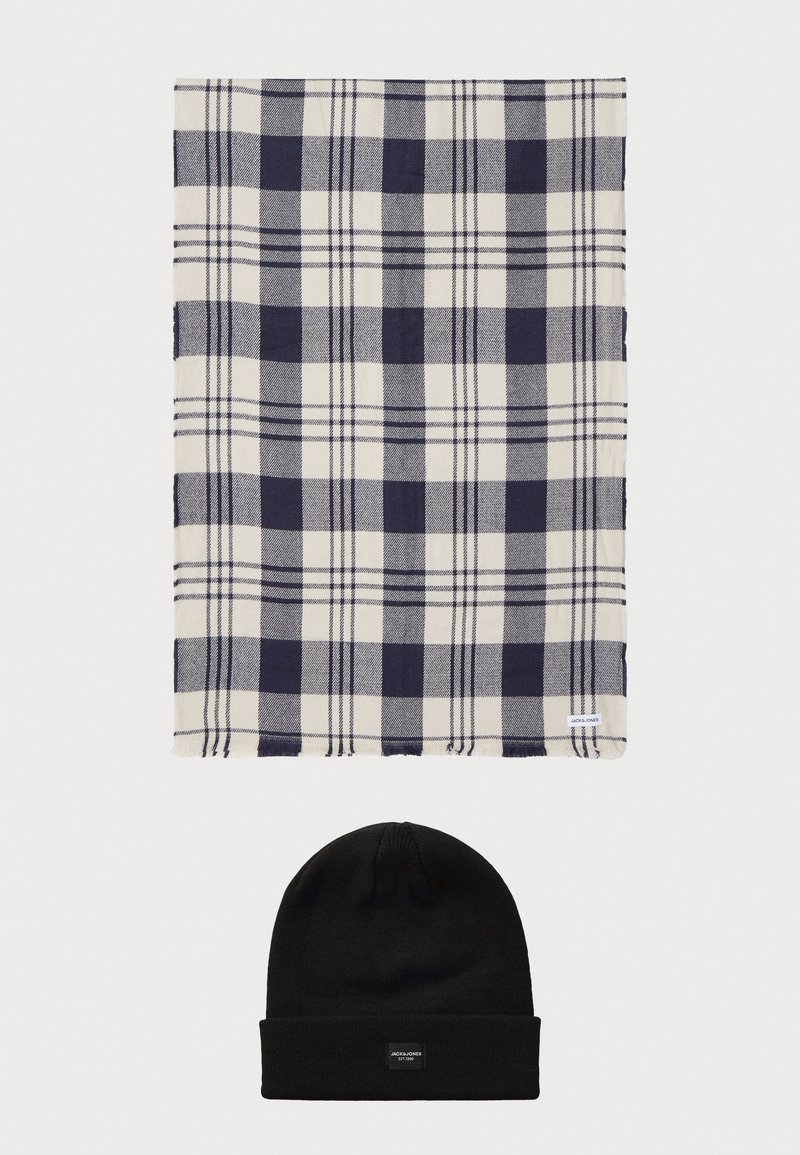 Ναυτικό μπλε και λευκό καρό κασκόλ με απαλή υφή πάνω από ένα μαύρο πλεκτό σκουφί. Το κασκόλ διαθέτει ετικέτα στην άκρη. Και τα δύο αντικείμενα είναι τοποθετημένα επίπεδα.