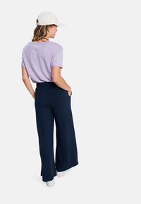 Ljuslila t-shirt kombinerad med marindöande vida byxor. Outfiten har fickor och kompletteras med vita sneakers och en keps.