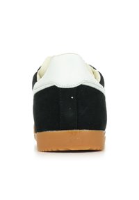 Sneaker nera in suede con tallone in pelle bianca, suola in gomma naturale, forma arrotondata, colletto imbottito e dettagli di cucitura rinforzati.