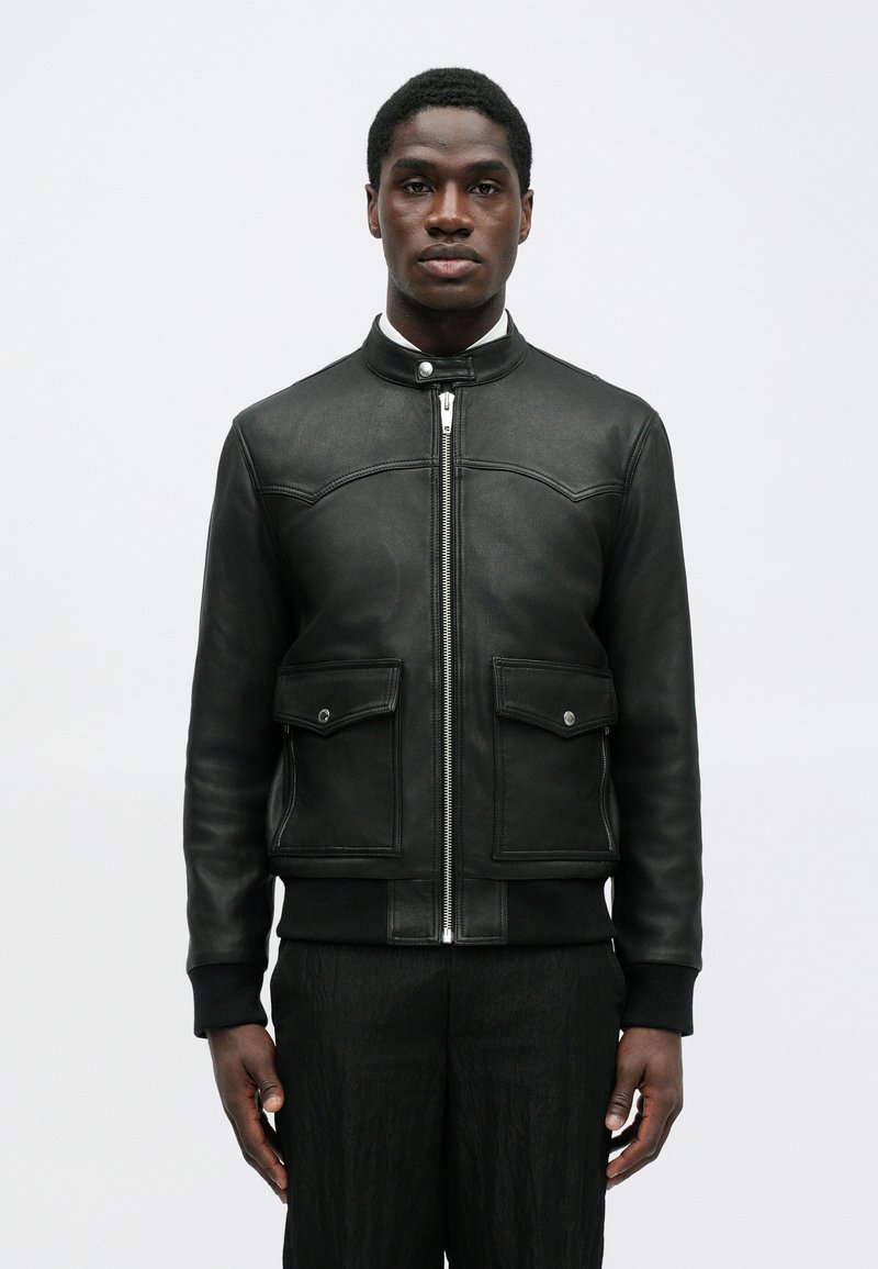 Black leather bomber jacket with a high collar, front zip closure, two chest pockets, and ribbed cuffs and hem; smooth texture.