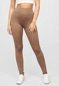 Leggings marron taille haute avec une texture douce et extensible, présentant une finition lisse et associés à des baskets blanches.