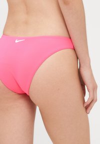 Rausvas bikinio apatinis trikotažas, pagamintas iš glotnaus audinio, turintis mažai kylančią dizainą ir mažą baltą logotipą nugaros pusėje.