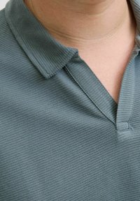 Polo en tissu texturé d'un bleu canard sombre, avec un col classique et une patte de boutonnage à trois boutons, mettant l'accent sur le col et la partie supérieure de la poitrine.