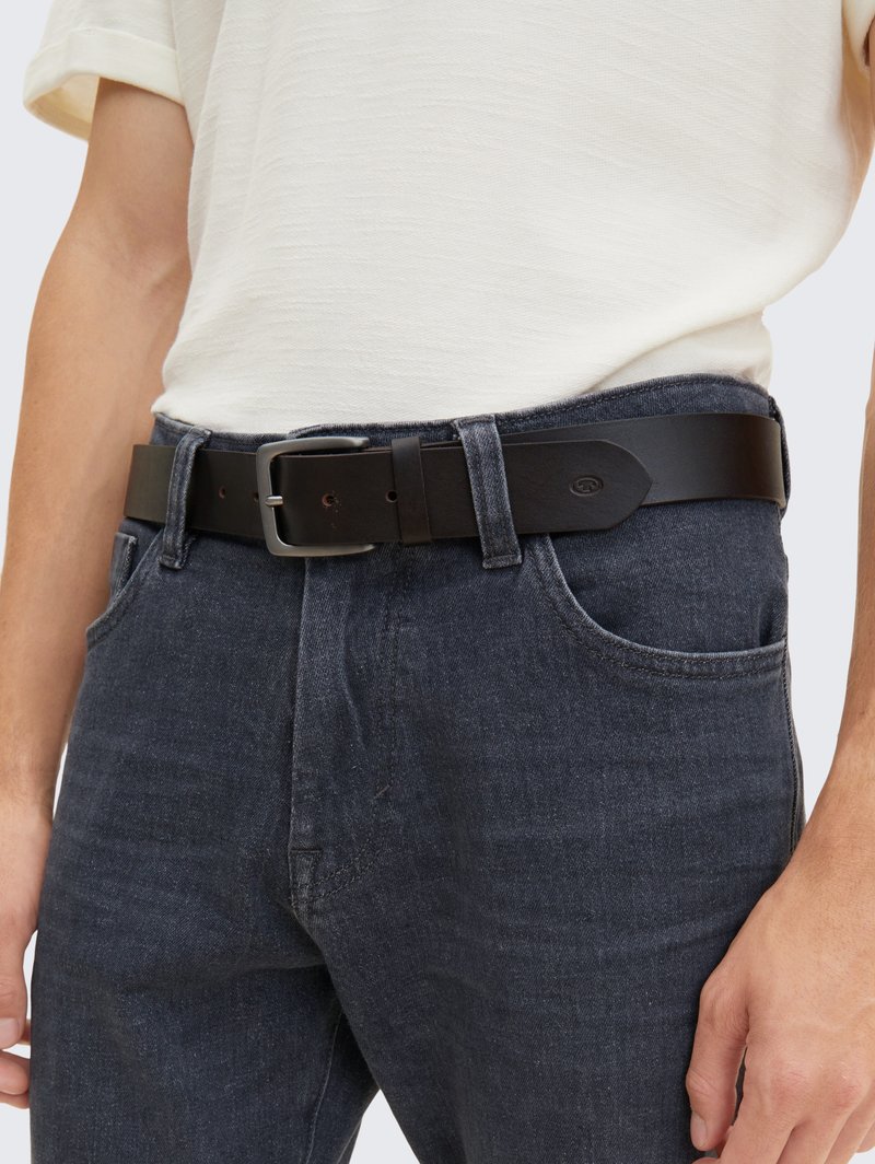 Black leather belt with a silver rectangular buckle, worn over dark blue denim jeans. The belt features a smooth texture and minimal detailing.