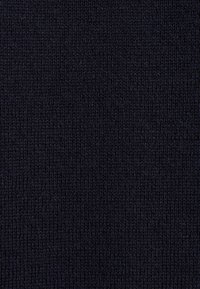 Gros plan sur un tissu noir tricoté montrant des rangées verticales de points et une texture douce.