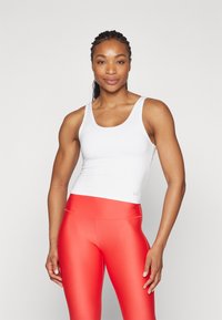 Fehér ujj nélküli trikó sima anyagból, élénk piros, magas derekú leggings-szel párosítva, fényes, rugalmas textúrával.
