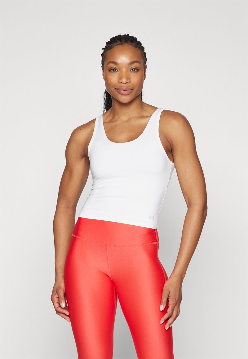 Fehér ujj nélküli trikó sima anyagból, élénk piros, magas derekú leggings-szel párosítva, fényes, rugalmas textúrával.