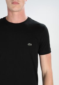 Black cotton t-shirt with a crew neck, featuring a small green and white embroidered crocodile logo on the left chest.