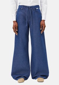 Dunkelblaue weite Jeanshose mit einem Kordelzugbund, verstärkten Taschen und dezenten Nähten. Glatte Stoffstruktur.