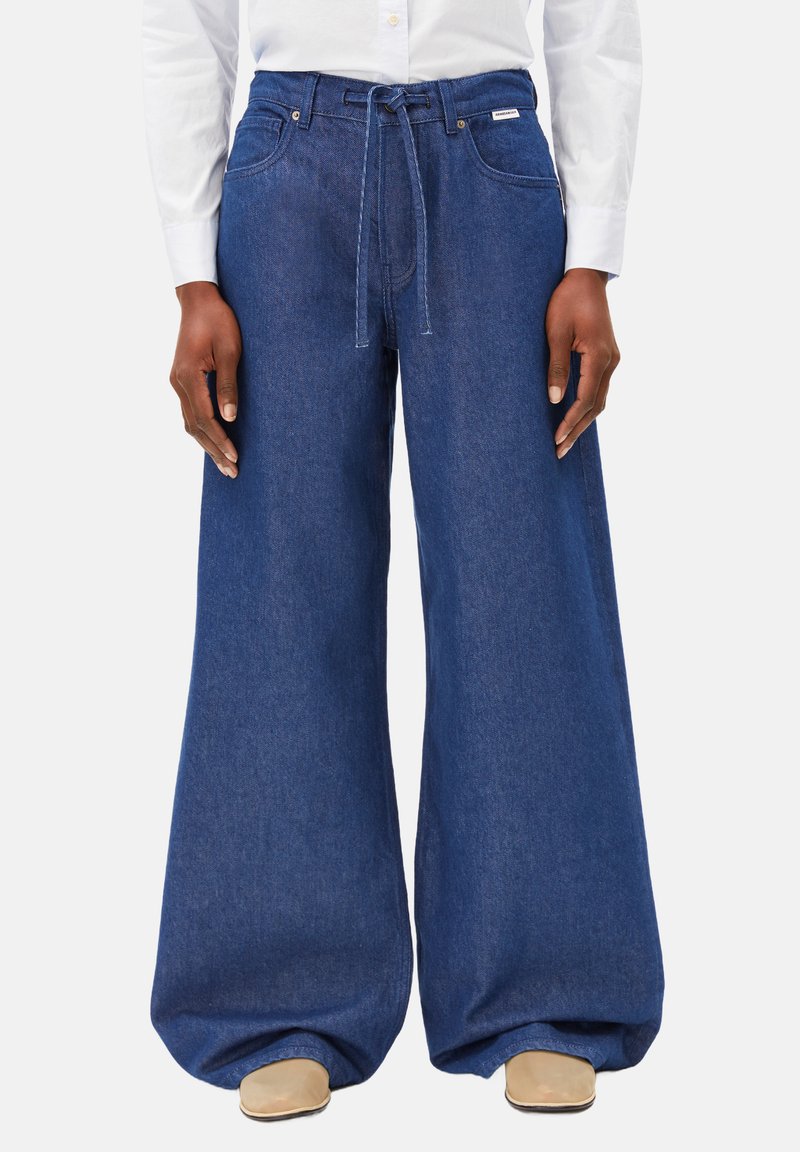 Dunkelblaue weite Jeanshose mit einem Kordelzugbund, verstärkten Taschen und dezenten Nähten. Glatte Stoffstruktur.